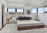 With window bands wrapping the room make the primary bedroom light and bright with views of the city beyond. A fattened wall with recessed shelf nooks for books, etc. supplants bedside tables. Additional closet to left and gloriette balcony to right (exterior).