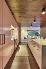 The wood flooring wraps up the walls and ceiling in the kitchen creating a "wood womb": A complimentary contrast to the the pink and sea-foam painted custom cabinets, brass hardware, brass backsplash and brass island. Windows were intentionally placed on both ends of the kitchen to create a cozy space.