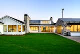 Painted white siding, zinc roof, stone, and a lush lawn offer a stunning portrait of color and texture. 