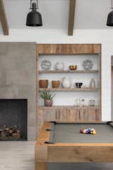 Concrete-look tile cladding on the fireplace is a smooth counterpoint to the reclaimed wood cabinets, which hide more party accoutrements. The wood-framed pool table also adds a rustic touch.