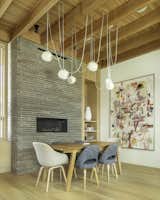 Dining room with modern chandelier, abstract art, linear bricks, and wood ceiling.