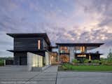 View from entry.  The view has a strong horizontal emphasis with its layering of foreground shoreline, river, distant shore, tree line and sky.  The house design compliments this view with layers of horizontal hovering elements: roofs, trellises and eaves.  The material palette is simple: dark woods, limestone, concrete and glass.