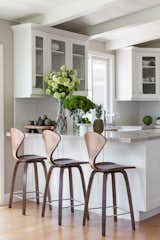 An all white kitchen with contemporary wooden barstools and pops of color complement this modern home.