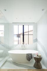 Bath Room, Stone Slab Wall, Light Hardwood Floor, and Freestanding Tub The master bathroom is another example of the intersection of rustic, raw materials, paired with the glamor of an oversized calacatta slab and a contemporary tub.  Photo 6 of 10 in Manhattan Ave Residence by Laney LA