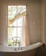 Many of the home’s furnishings are made from recycled materials, vintage finds, or nearly new pieces—such as this bathtub, which Jessica salvaged from a renovation at a friend’s house. The curtain was made from a vintage French sheet, which ironically—for a bathroom—has the initials BM embroidered on it.&nbsp;