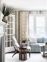 Kevin Isbell selected pinch-pleated, block-print linen curtains with tape trim on the leading and bottom edges, hung from blackened metal rods and brass rings for this calm, clean living room.