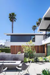 The volume of the house is a two-story stucco façade structure with vertical cedar and black metal accents. Stack bond CMU garden walls in the front yard define the entry sequence, honoring the mid-century history of the residence.