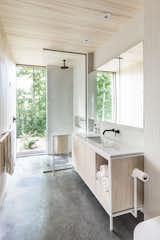 Concrete stretches across the bathroom floor into the shower, where a floor-to-ceiling window frames the great outdoors. A simple palette of concrete, plywood, and keystone white mosaic tile gives the bathroom a clean look.