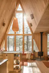 In Hannah’s initial sketch of the house, she drew an A-frame with a floor-to-ceiling windows in the front. “It was important to have that tall ceiling in the living space and all the light,” she says. In the front living room, a maple pendant light from Modern Maine crowns the space. And a locally manufactured Jotul stove warms the space. A 84-inch projector screen was installed parallel to the sliding door, so the couple can tuck it away during the day and at night pull it down to watch movies.