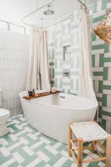 The bathroom features a soaking tub by American Standard with Grohe fixtures, including a rain showerhead. Though she's not much of a bath person, she wanted to make it feel like a retreat with a personal spa. "The soothing color palette from Fireclay Tile plus little touches from The Little Market really set the tone...I made sure to include my favorite skincare and haircare products by True Botanicals and Parachute Home. The little bath tub tray has a lovely candle, matches, bath salts, even a little notch to put your glass of wine—everything you need for a long, luxurious bath." She tops it off with an abundance of fluffy towels from Parachute. A large vanity has Semihandmade walnut covers, connecting the modern bathroom to the wood textures found throughout the cabin.