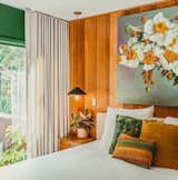 "I love the view from our bed, and had this idea of bringing the outside in through color," says Thomas. "I painted the room a rich, emerald green—Mission Jewel by Dunn Edwards—and centered the color palette on a painting by Michael Harnish of a floral arrangement by my dear friend, Yasmine Khatib." Black-and-brass Mitzi pendants float above the nightstand, while two chairs she reupholstered with Kravet velvet sit in the corner to match the dark walls. Floor-to-ceiling drapes by The Shade Store add a touch of drama. 