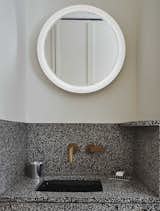 The intricate, speckled design of the vanity is paired with clean white walls and an illuminated circular mirror.