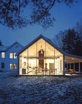 The Floating Farmhouse’s semitransparent addition has a roofline that matches the pitch of the original 1820s farmhouse. A porch, tucked under the side eaves, is cantilevered over a stream that runs through the property. Ikea loungers are illuminated from the interior by commercial gymnasium lights repurposed as pendant lamps.