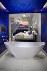 Orienting the master suite along the rear of the home and providing floor-to-ceiling glazing allows homeowners to fall asleep looking at the twinkling lights. Rather than closing the master bath off from the views, designers opted to create an enclave, connecting the bedroom and bathroom, in which to place the deep soaking tub. A pop of color delineates the space uniquely from both the bedroom and the rest of the bathroom area.