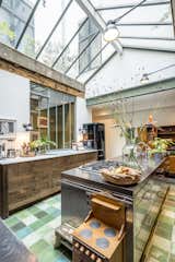 On a sought after an idyllic island in the center of Amsterdam an old warehouse, formerly in use as a pillow factory and a garage has been converted to a warm and eclectic family home. The kitchen features a mixture of green tiles, green painted mullions, and exposed wood beams for a warm, soft feeling that contrast sharply with the more industrial stainless steel island. The kitchen island incorporates a stove top and storage, and benefits from natural light from the skylight overhead.