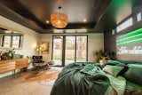 The master bedroom includes a vintage Eames chair and cowhide rug, along with an oversized bed and custom neon headboard.
