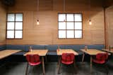 Dining Room, Bench, Chair, Table, Pendant Lighting, and Concrete Floor Red chairs lend a pop of color against rich oak walls, and walnut and leather banquets.  Photo 4 of 8 in An Australian Cafe Filled With Handcrafted Details Comes to Portland, Oregon