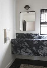 A dramatic black and gray marble brings subtle glamour to this petite powder room, which was originally designed in the 1920s by noted female architect Frankie Faulkner. Dark&nbsp; floor tiles and accessories like a black-framed mirror and dark window treatments tie the black-and-white theme together.