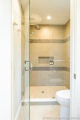 The minuscule primary bathroom in this California condo illustrates how glass shower doors visually impact a room’s appearance. The frameless glass doors open the space up, making it feel much larger than it is. Homeowners Terry and Steve wanted a clutter-free aesthetic; incorporating towel bars into the glass doors and adding only small hooks to the wall makes the bathroom more luxurious.