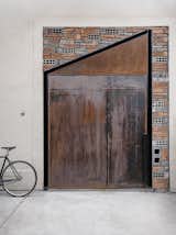 Doors, Metal, Swing Door Type, and Exterior Reclaimed bricks and a pivoting, weathered steel door speak to the industrial flavor and salvaged materials found throughout this office renovation by architecture studio Linehouse. The result is a design that is both dramatic in form and texture, but subtle in its natural palette.  Photo 6 of 12 in Herschel Supply's New Shanghai Office Revives the Lane House Style