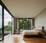 Bedroom, Bed, Chair, Recessed, Night Stands, Rug, Medium Hardwood, Floor, and Lamps The bedroom on the second floor has a treehouse-like feel.  Bedroom Lamps Chair Bed Recessed Rug Photos from This Concrete Abode Embraces Indonesia's Tropical Climate