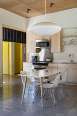 Plywood cabinetry and ceiling panels have been combined with white walls to create a clean kitchen setting. A Modernica Nelson Bubble Lamp hangs above the dining table. 