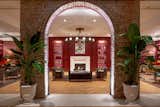 An original brick wall with an arch opening frames views of The Press Room, a cozy lounge lined with paneled walls painted a deep cranberry hue to match the Press Room bar front.