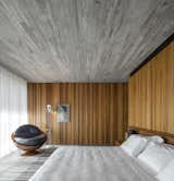 Bedroom, Concrete Floor, Bed, Chair, Floor Lighting, Table Lighting, and Rug Floor The interiors feature a minimal palette of timber and concrete. The bathroom of this bedroom is hidden behind a sliding wall.   Photo 5 of 16 in An Expansive Grass Roof Tops This Modern Brazilian Home
