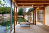 The entry foyer—perched on the pond’s west bank—opens to a long, glazed walkway, which is elevated above the water and leads to the main living spaces and bedrooms beyond.