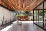 Outdoor, Shrubs, Hardscapes, Back Yard, Tile Patio, Porch, Deck, Small Patio, Porch, Deck, Trees, Concrete Fences, Wall, and Gardens Protected from prying eyes by a planted slope, the back of the property soaks up the sun with a hammock hung from the ceiling.

  Photos from A Modern Mexican Home Rises With Vertical Timber Cladding
