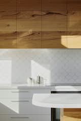 The kitchen's overhead cabinets have been built from solid timber recycled from re-milled Messmate hardwood floorboards. The dainty scallop tiles cover the kitchen backsplash, giving the space a visual identity.