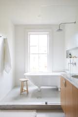 A clawfoot tub was installed beneath the window and can be seen from the bedroom. The semi-enclosed shower room is lined in white subway tile while sage green penny tiles cover the floors.