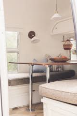 Dining Room, Medium Hardwood Floor, Wall Lighting, Bench, Ceiling Lighting, and Table The table in the dining area folds down to make a bed; however, Bonnie says that the family actually prefers to sleep together in the convertible sofa area.  Photos from Before & After: Bold Wallpaper Brings Dreamy Vibes to a Dated Airstream