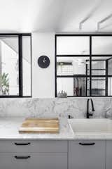 Kitchen, Drop In, Porcelain Tile, Engineered Quartz, White, Accent, and Wall The kitchen overlooks views of the outdoors and the study.  Kitchen Drop In Wall White Accent Photos from Budget Breakdown: A Stunning Apartment Revamp Mixes High and Low For Under $100K