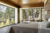 Bedroom, Bed, Table Lighting, Wall Lighting, and Medium Hardwood Floor The master bedroom was crafted with a low wooden ceiling to create a sense of intimacy, balancing out the expansive walls of glass on two sides.

  Photos from This Modern Cliff House Seamlessly Knits Into a Rocky Idaho Lakefront