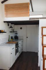 Kitchen, Subway Tile, Wall, Laminate, Medium Hardwood, White, Wall Oven, Refrigerator, and Cooktops The loft bedroom is located above the galley kitchen and bathroom, and is accessed via stairs with built-in shelving.  Kitchen Laminate Cooktops Subway Tile Photos from Budget Breakdown: A Maui Couple Build an Off-Grid Tiny Home For $45K