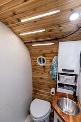 The bathroom is outfitted with a Nature's Head composting toilet, stainless steel sink, and custom cabinets. The countertop and curved wall are built from cedar. The LED lighting strips add a modern touch. 