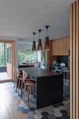 The kitchen was opened up to make way for more counter space and a large island. All appliances were updated with Bosch products. "The client was interested in a simple material and color palette of white oak uppers, matte black lowers with Corian countertops, and white gyp walls accentuated by patterned tiles," the architects say. The pendant lights are by Secto design and the bar stools by Cherner.