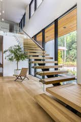 The sculptural stairway is fitted with white oak floating treads, a steel stringer, and a glass guardrail.