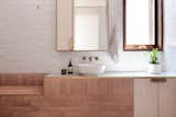 The bathroom walls are lined with Surface Gallery Flake White Ceramic tiles and paired with brick. The tapware is Astra Walker Icon Basin Mixer in Eco Brass. 