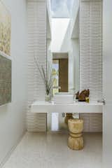Bathed in daylight, the powder room includes Heath Ceramics wall tile and a custom slab vanity and mirror.