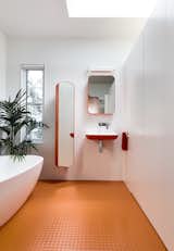 A skylight illuminates the master bathroom, which is entirely outfitted with Arblu Tulip fixtures. The orange floor is Kenbrock K2 studded rubber. Note how the divisional wall stops short of the ceiling—a decision that the architects implemented to "create volume and height, which celebrate the curve of the ceiling."
