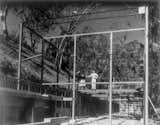 Ray and Charles Eames seen standing on the steel frame of the house, which consist of two rows of 4-inch H-columns set 20 feet apart. A 12-inch open-web joist forms the top member.