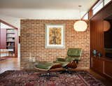 The west brick wall continues to the interior and serves as an accent wall dividing the entry hall from the living room. A corner of the room is furnished with an Eames lounge chair, a Nelson Bubble Lamp, and a Silas Seandel coffee table.