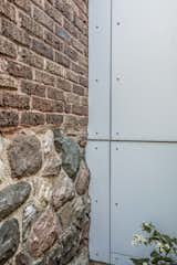 A close-up look at how the laser-cut steel panels meet the rough field stone and brick foundation of the existing house.