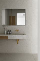 A solid terrazzo sink juts out from the wall with an integrated wooden drawer. The mirror conceals an oak cabinet.