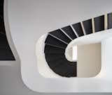 Built to replace a traditional rectangular stairway, the curving open-riser staircase features extra-wide black treads that pop against white guardrails.