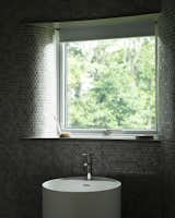 A peek inside the downstairs bathroom, which is covered in mosaic tiles that echo the microcement finish used throughout the home. "As it is a north-facing room, matte and gloss finishes have been employed to play with reflections from sunlight as it enters the space," note the architects.