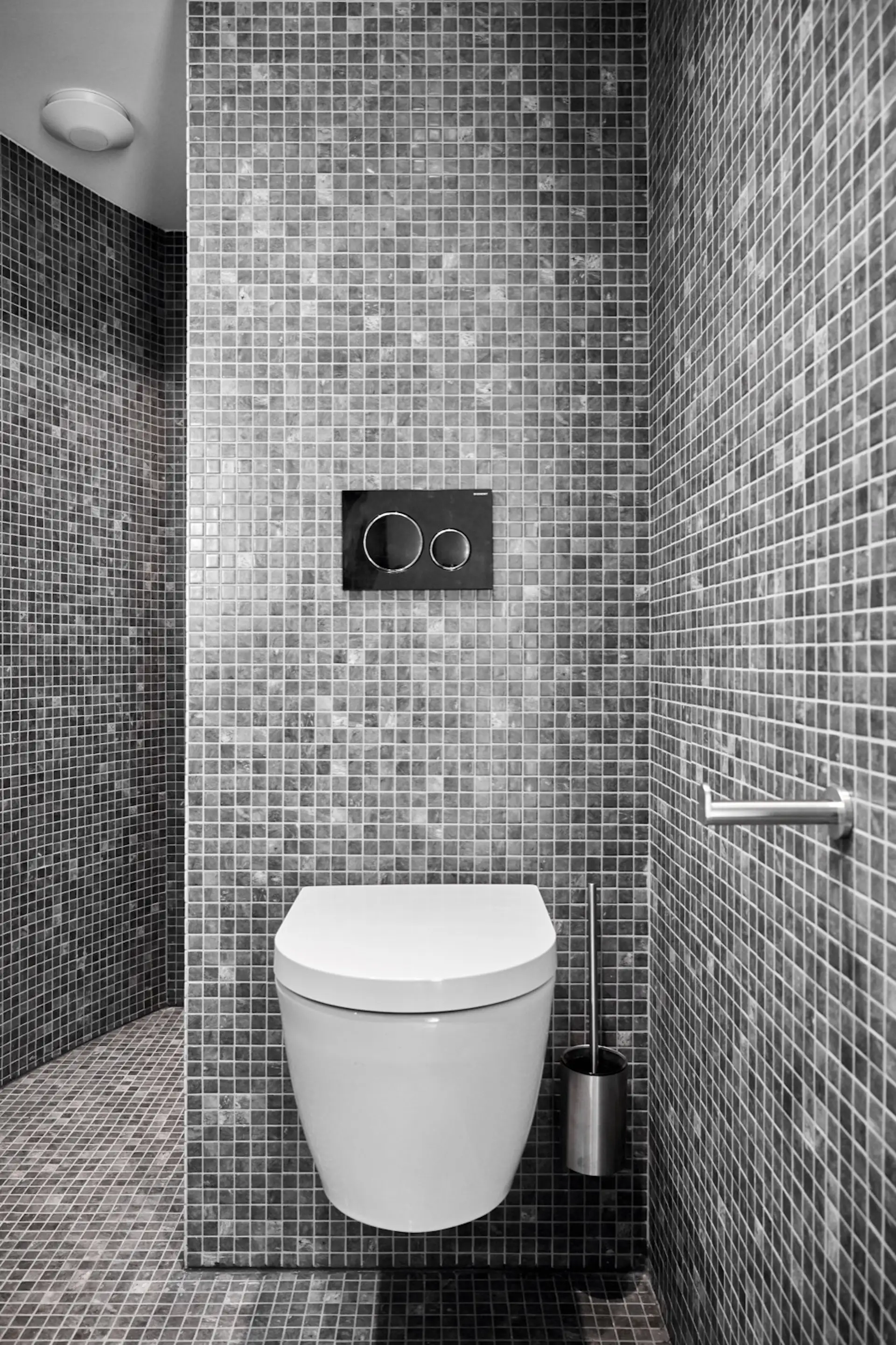 The bathroom is fitted with a dual-flush toilet, shower, and sink. Ceramic mosaic tiles line the walls and floor.