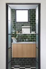 The main bathroom in Emerald green subway tiles and black & white checkers-like flooring give a fresh yet classic backdrop for plants, and cosmetics.